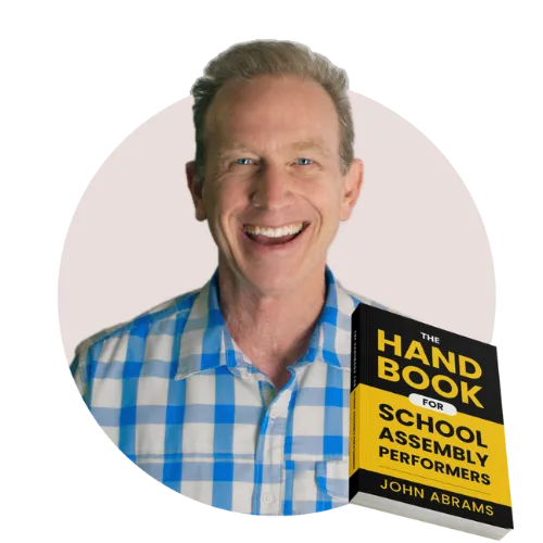 John Abrams smiling next to his book The Handbook for School Assembly Performers