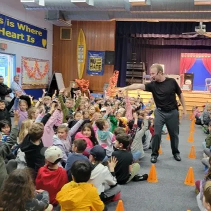 Performer pointing to excited students with raised hands during school assembly show