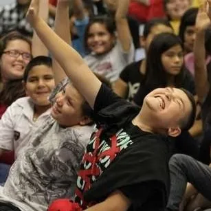 Excited students with their hands raised eagerly during a STEAM Magic school assembly