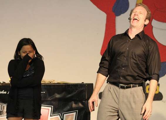 "Student and school assembly presenter laughing together on stage during a comedic and uplifting performance."